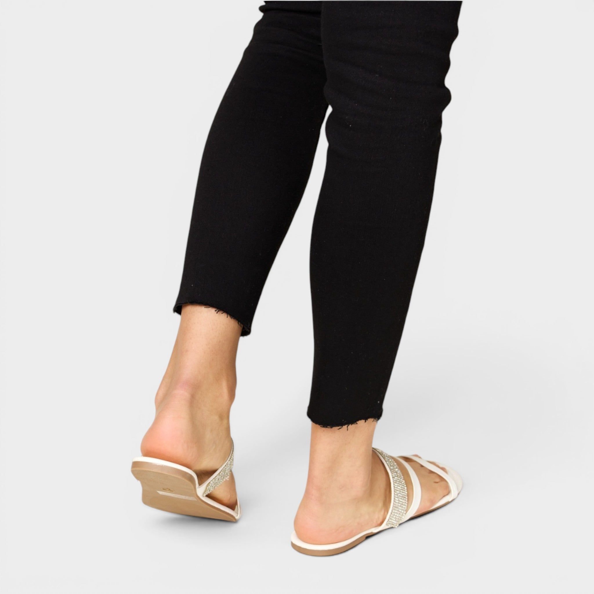 Person wearing black pants and beige sandals on a light gray background