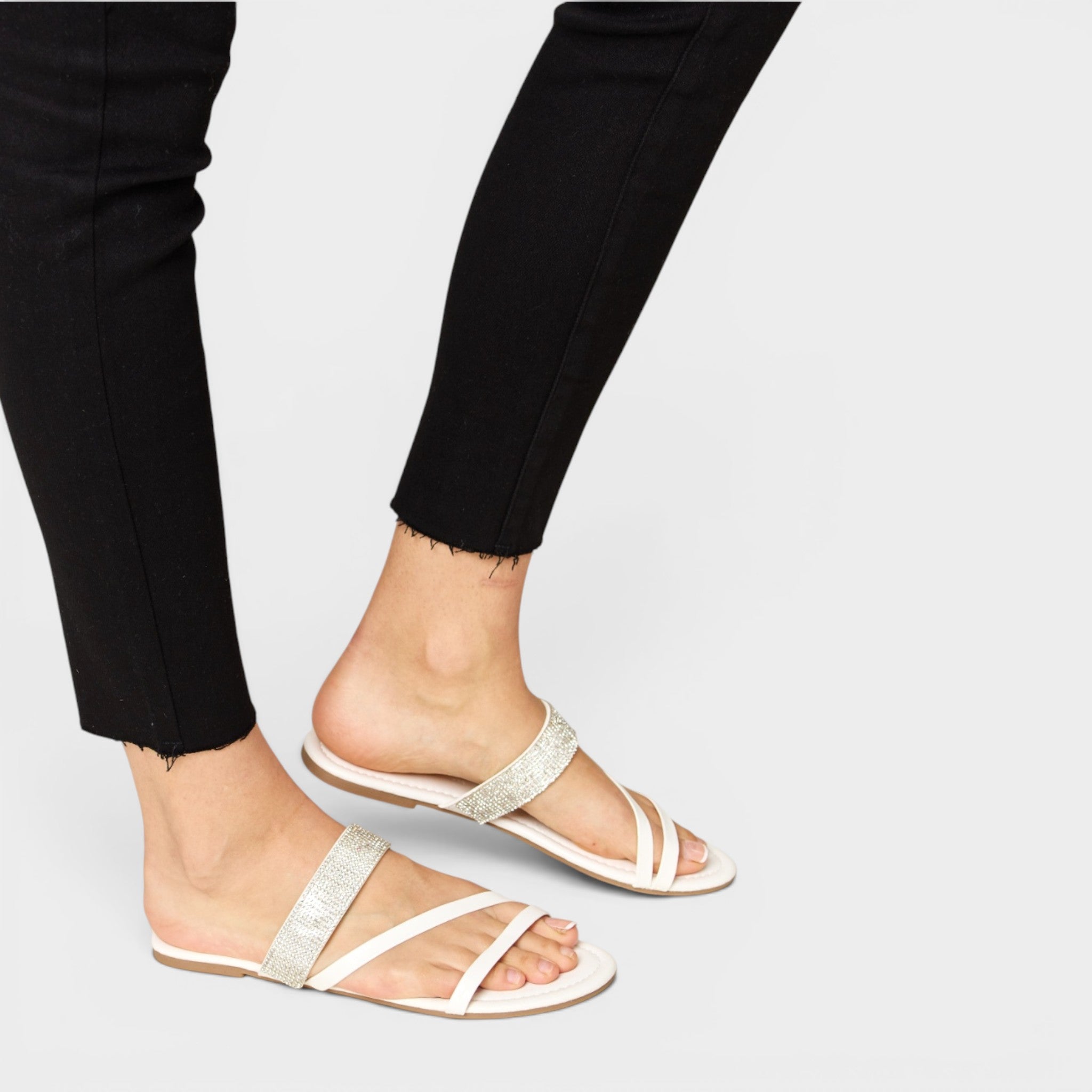 White sandals worn with black pants on a light gray background