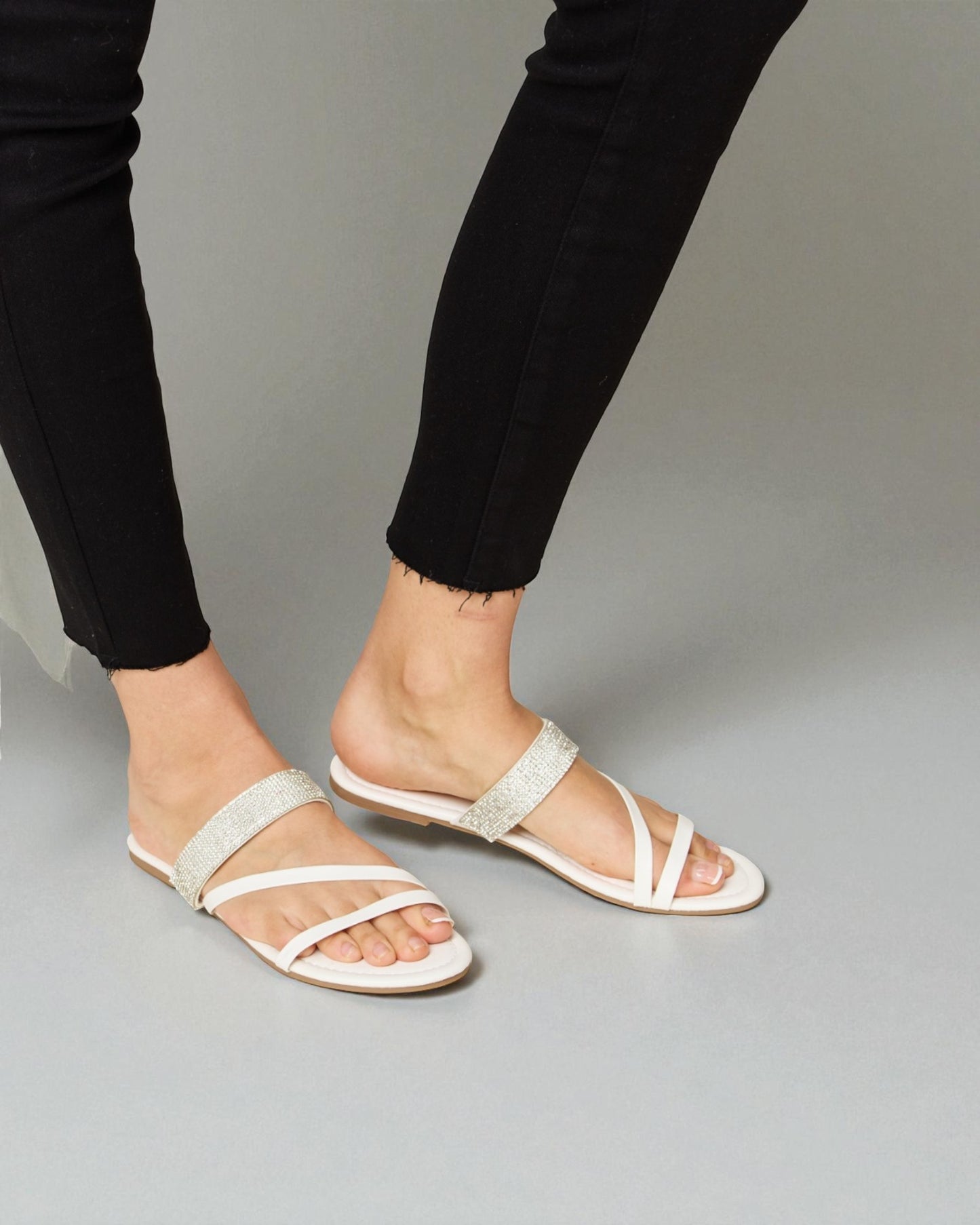 White sandals worn with black pants on a gray background