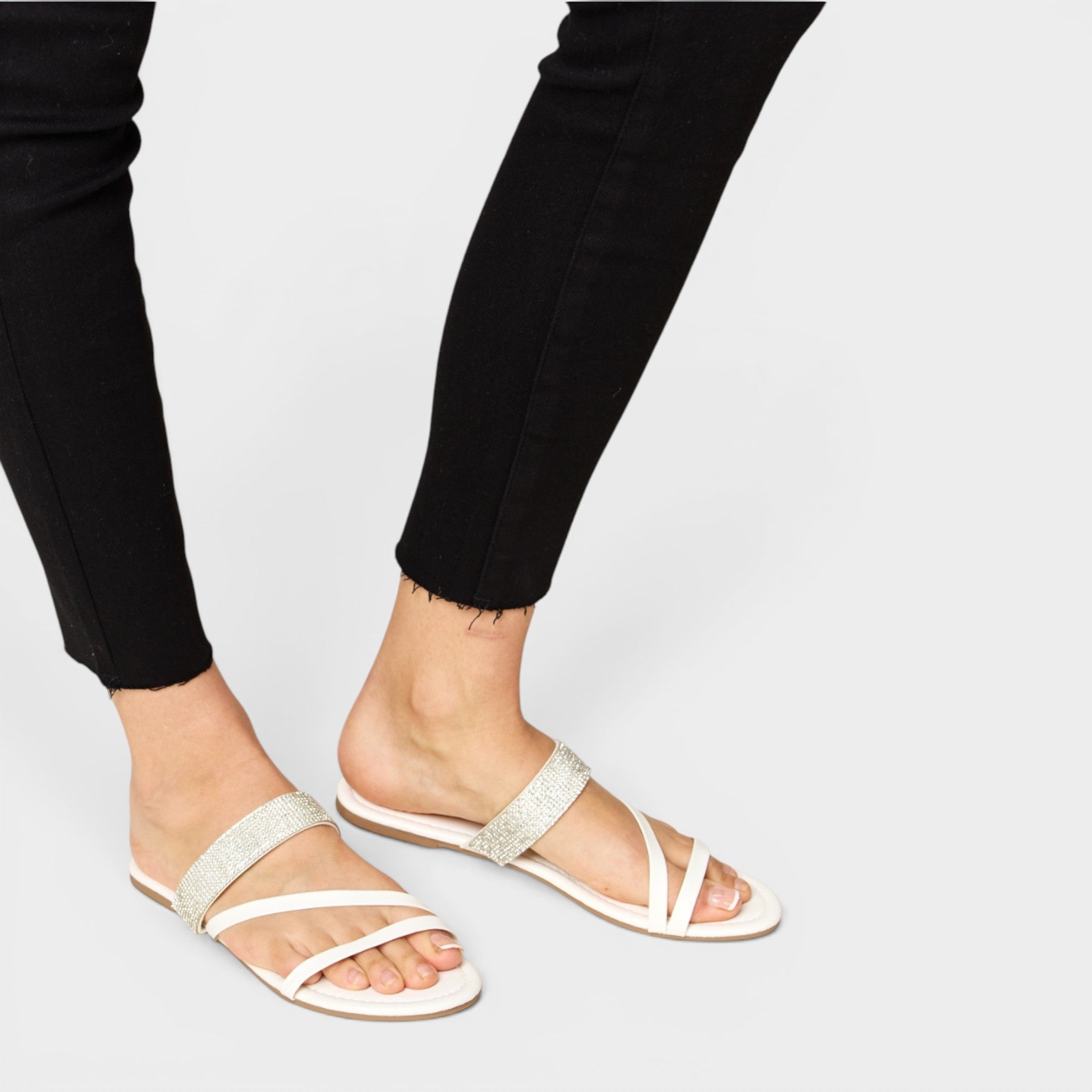 White sandals worn with black pants on a light gray background