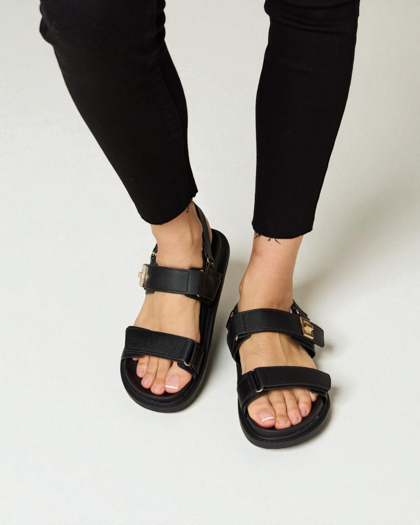 Black sandals worn with black pants on a plain background