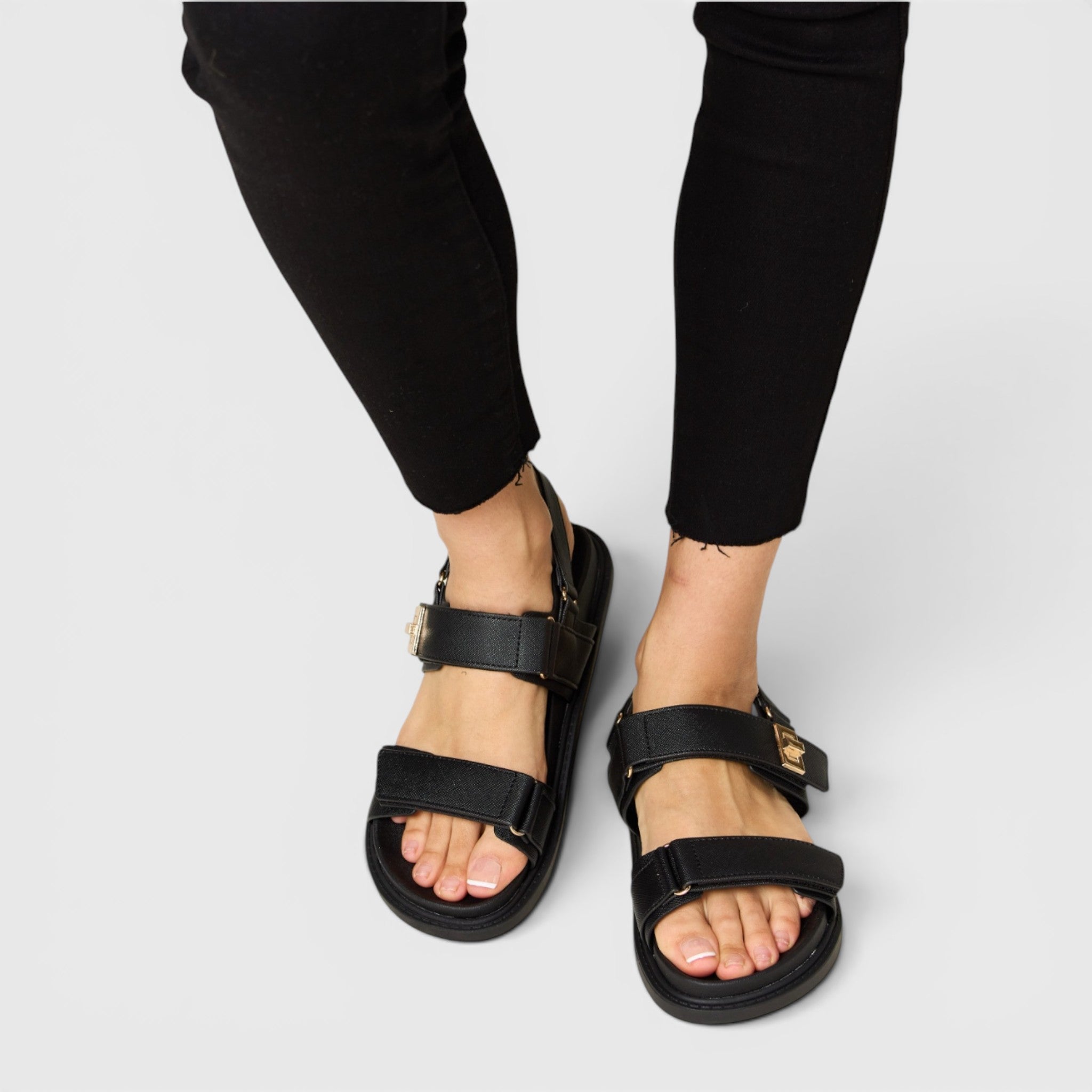 Black sandals worn with black pants on a light gray background