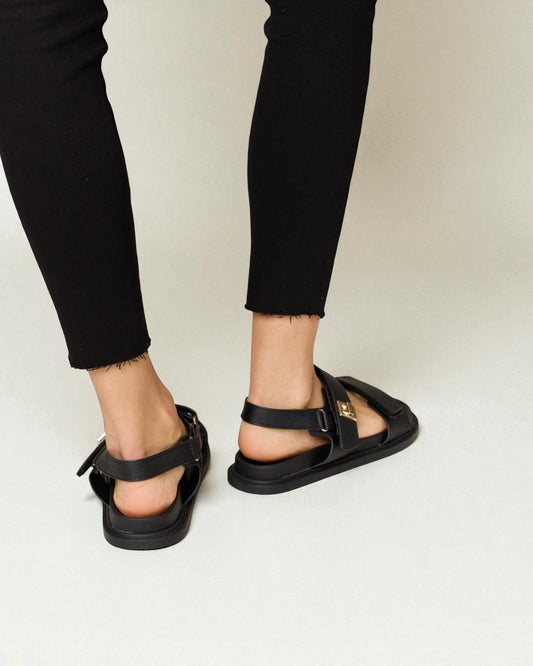 Black sandals worn with black pants on a plain background