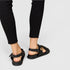Black sandals worn with black pants on a light gray background
