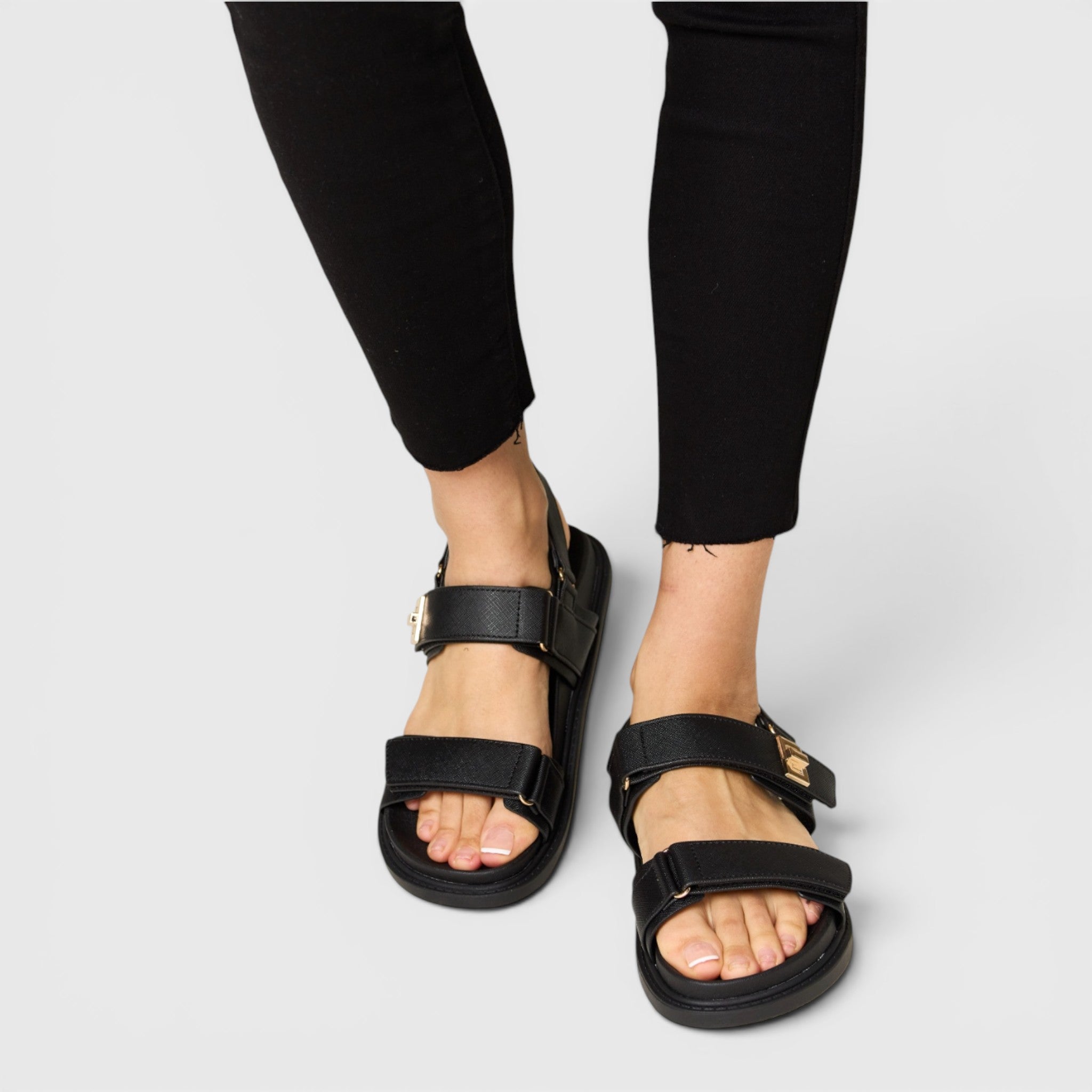 Black sandals worn with black pants on a light gray background