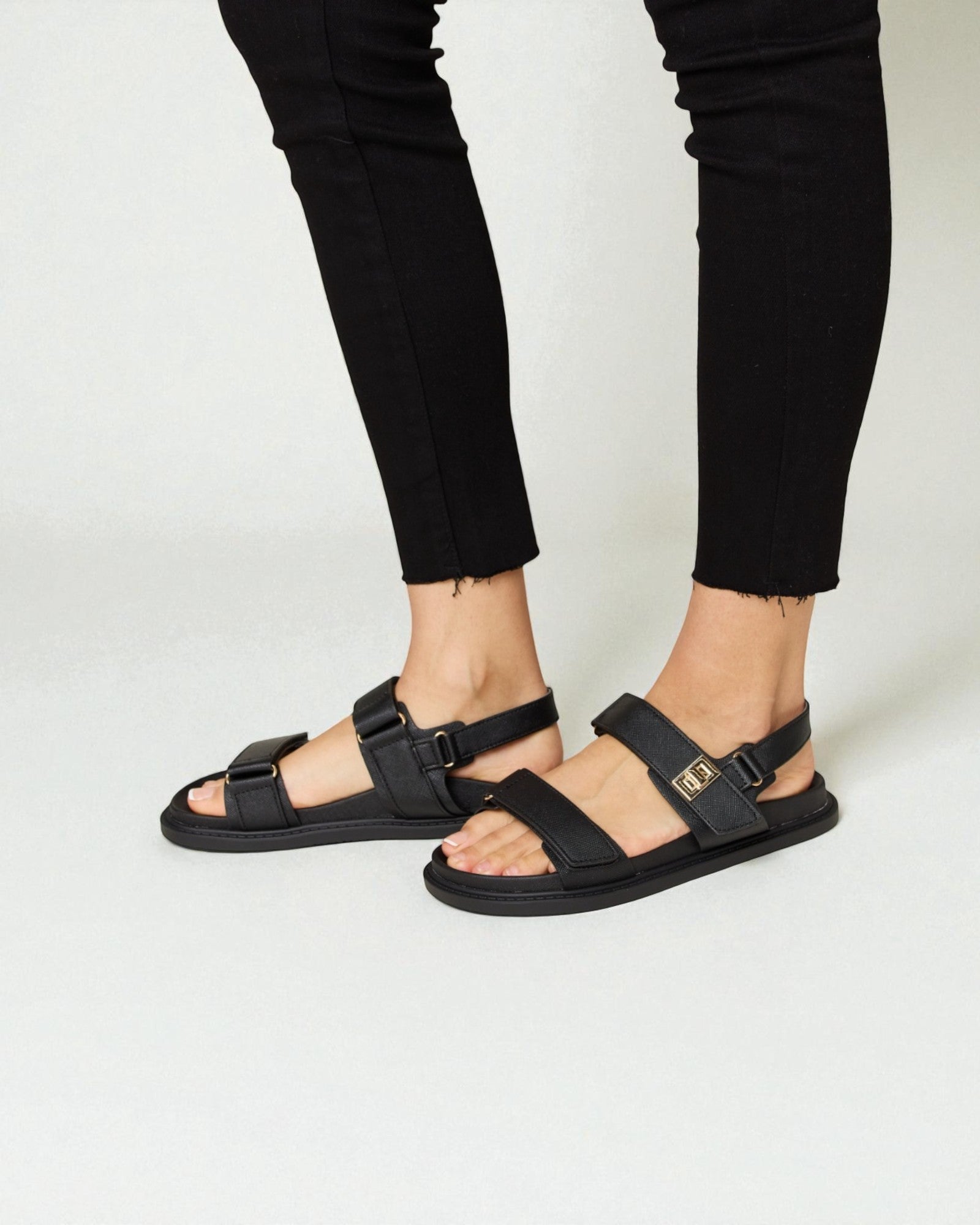 Black sandals worn with black pants on a white background