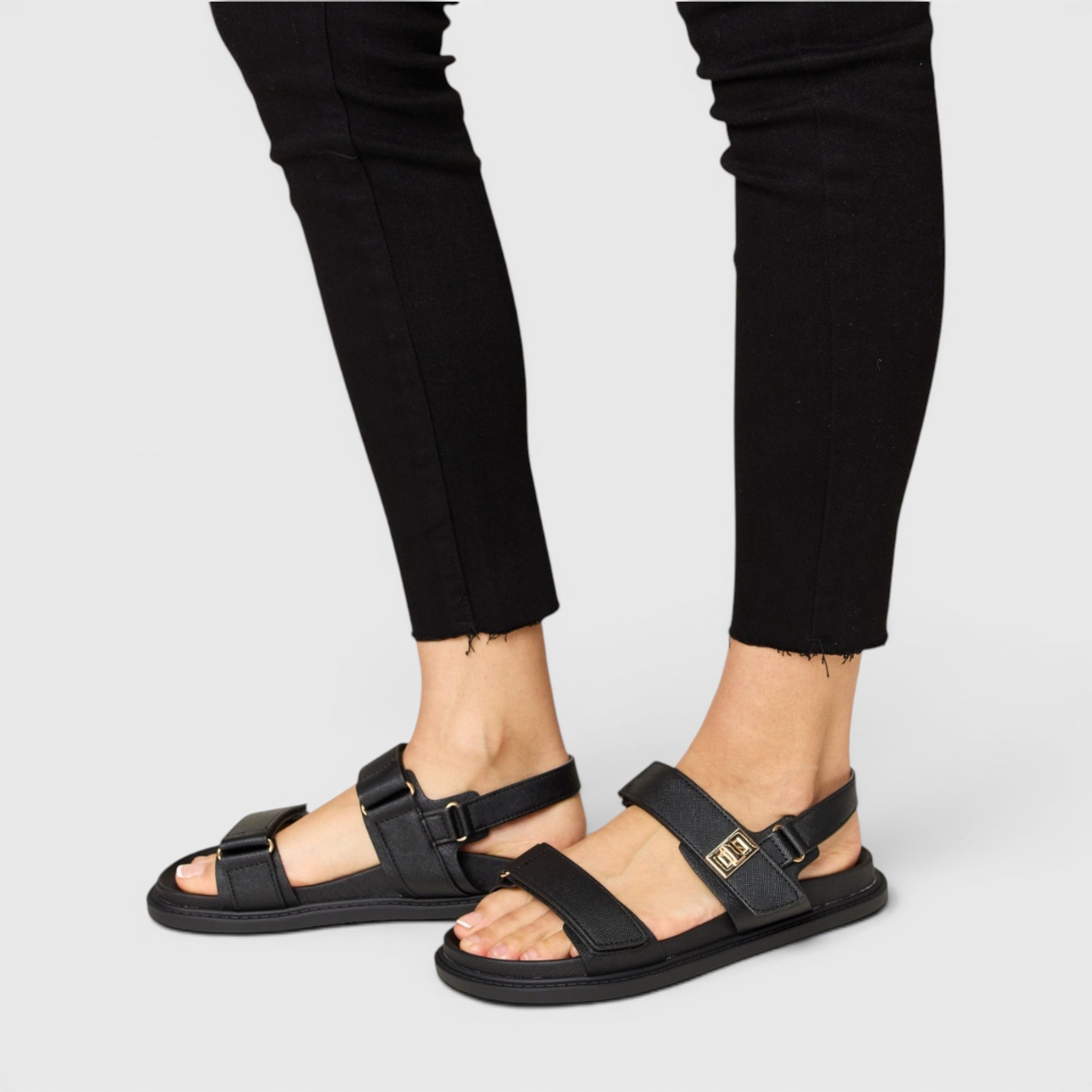 Black sandals worn with black pants on a light gray background