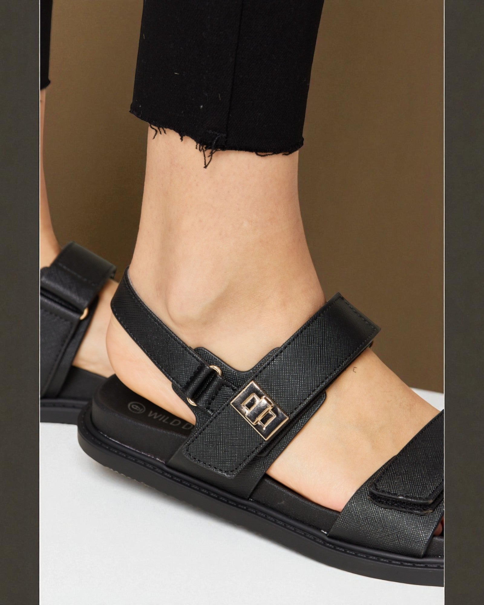 Black sandal with a gold buckle on a neutral background