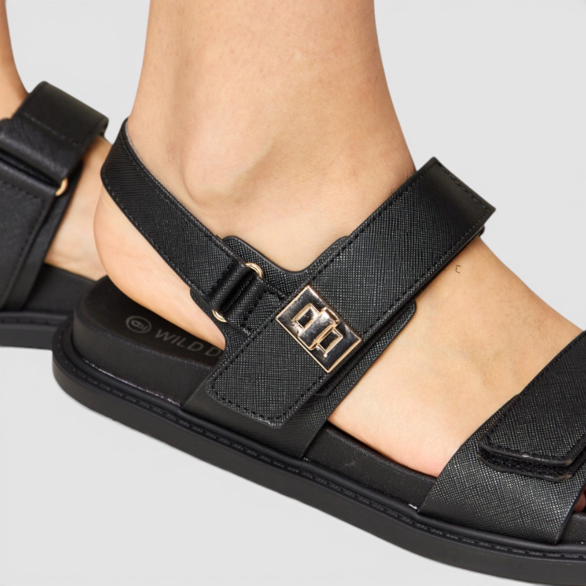 Black sandal with a gold buckle on a light gray background