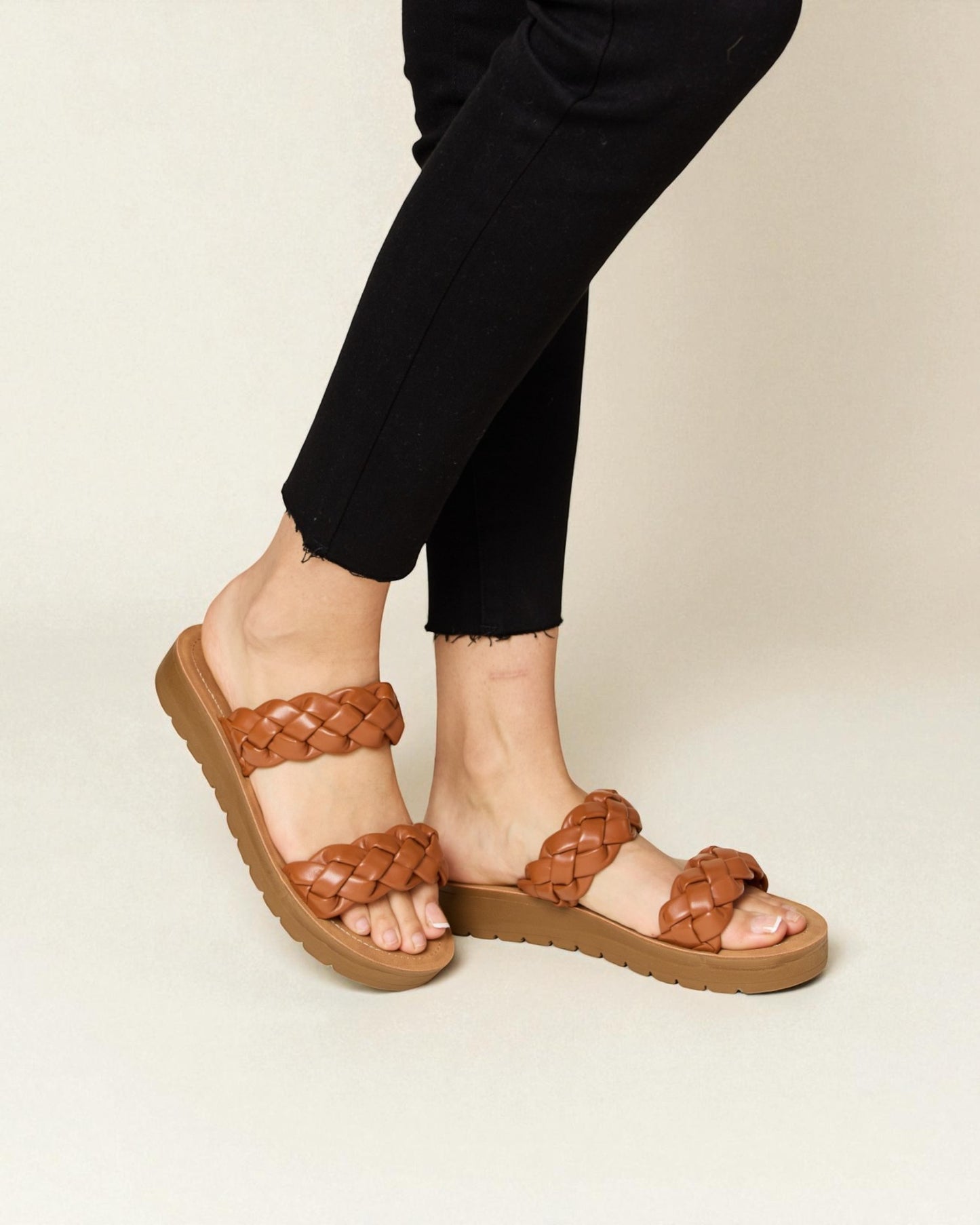 Brown braided sandals worn with black pants on a beige background