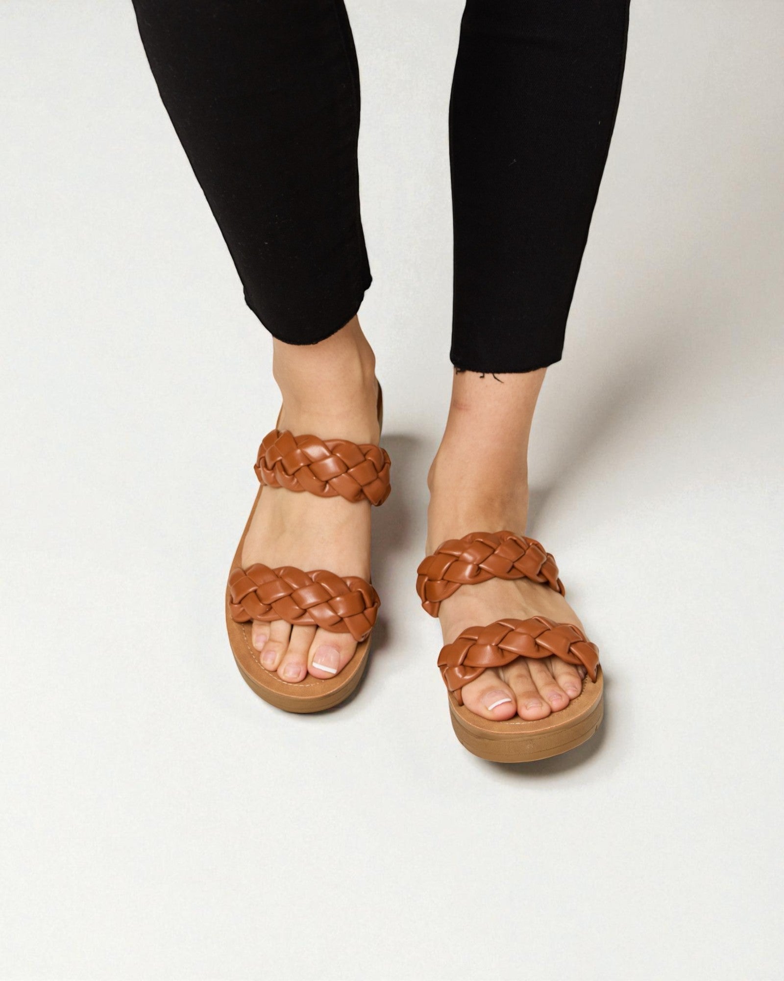 Brown braided sandals worn with black pants on a white background