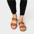 Brown braided sandals worn with black leggings on a light gray background