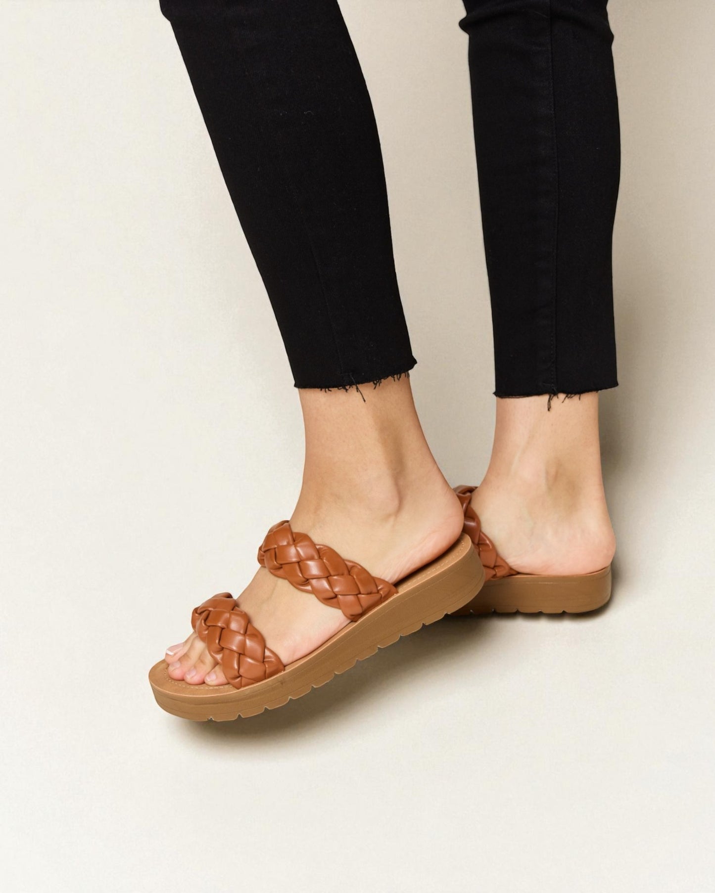 Brown woven sandals worn with black pants on a neutral background