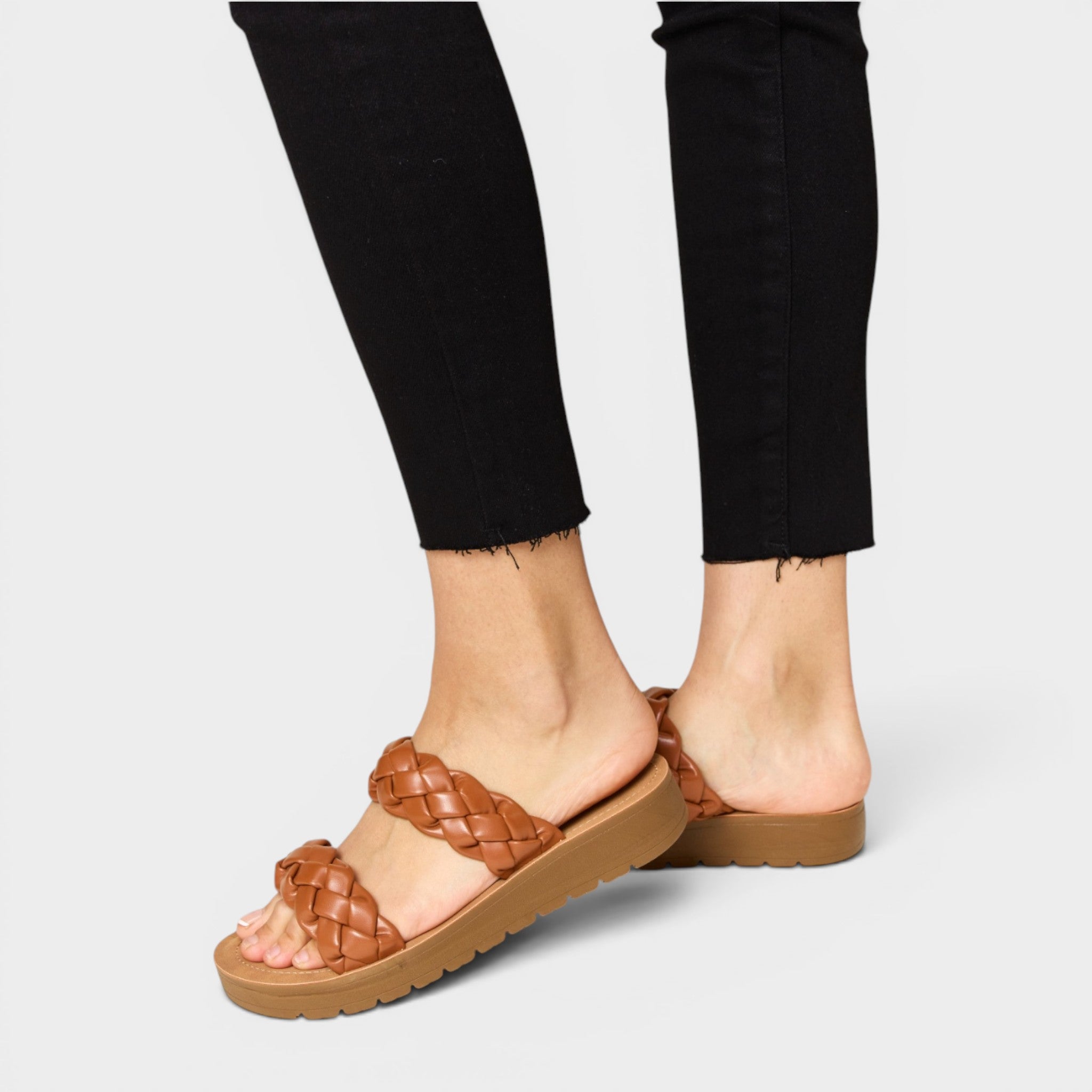 Brown woven sandals worn with black pants on a light gray background