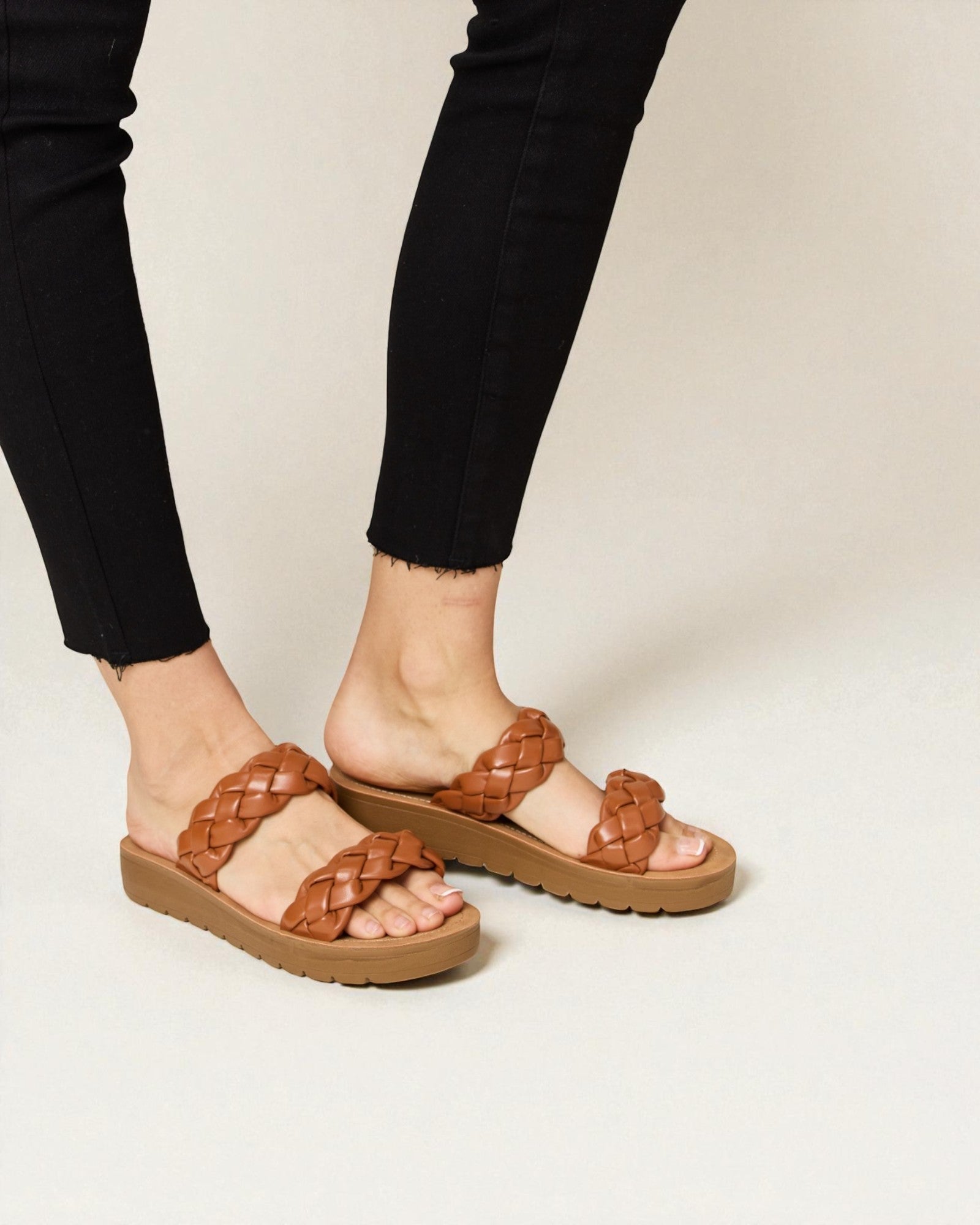 Brown woven sandals worn with black pants on a neutral background