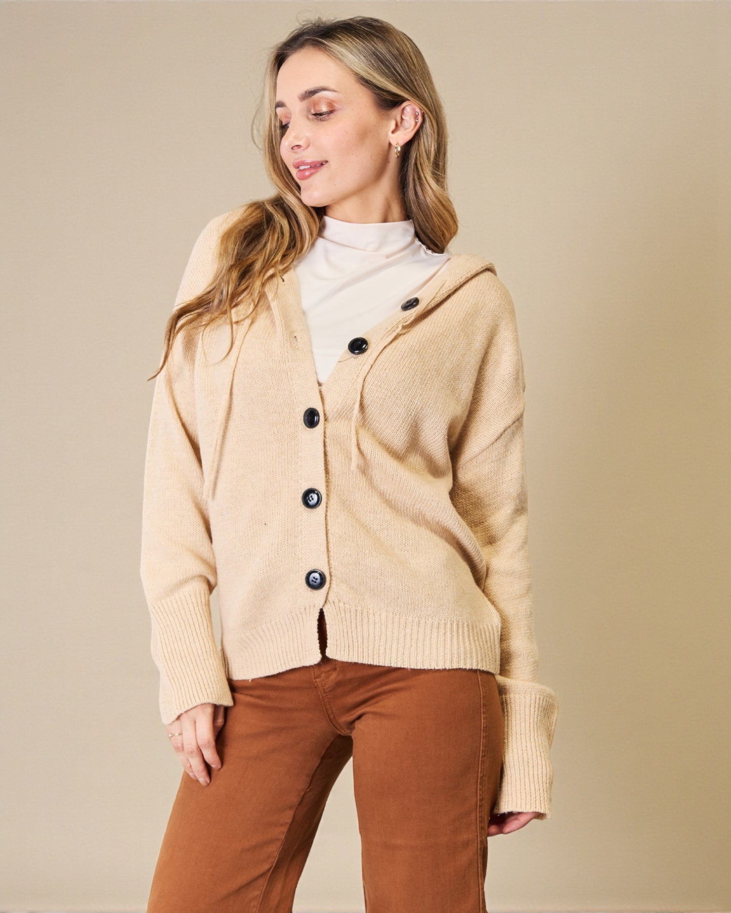 Woman wearing a beige cardigan with black buttons on a beige background