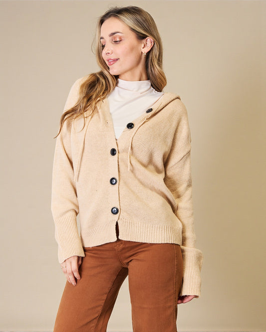 Woman wearing a beige cardigan with black buttons on a beige background