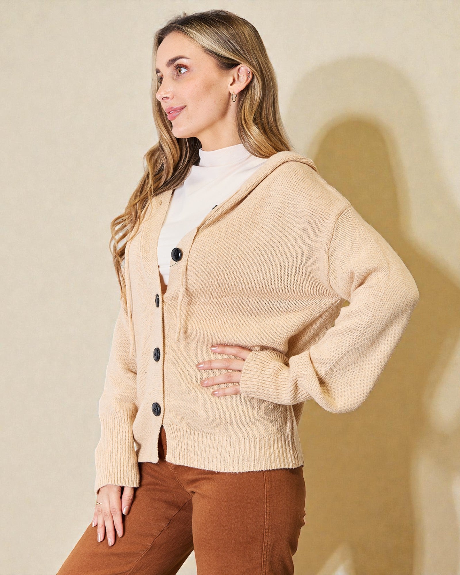 Woman wearing a beige cardigan with black buttons against a plain background
