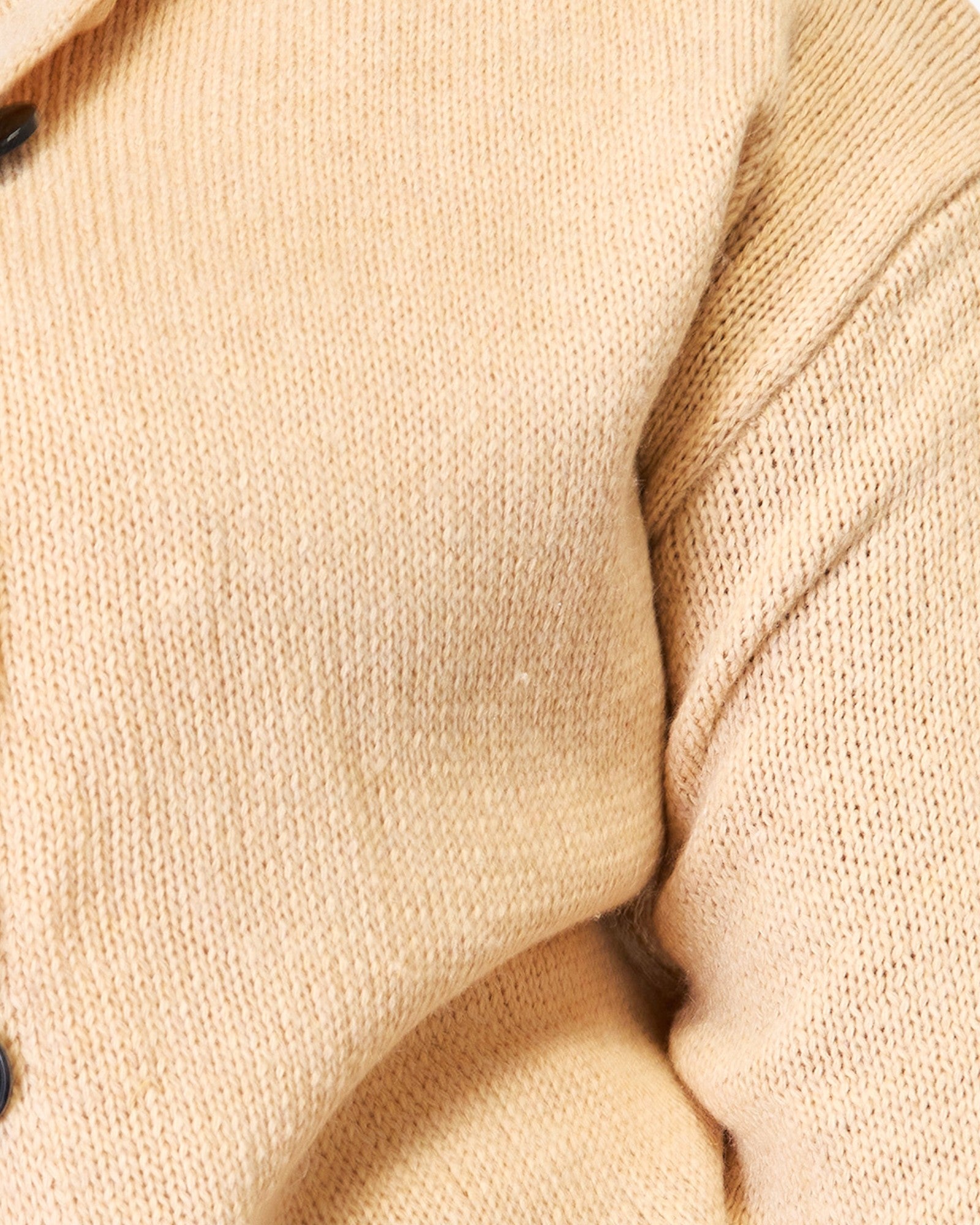 Close-up of a cream or light beige knit fabric, showing the detailed texture of the knit pattern and soft folds.