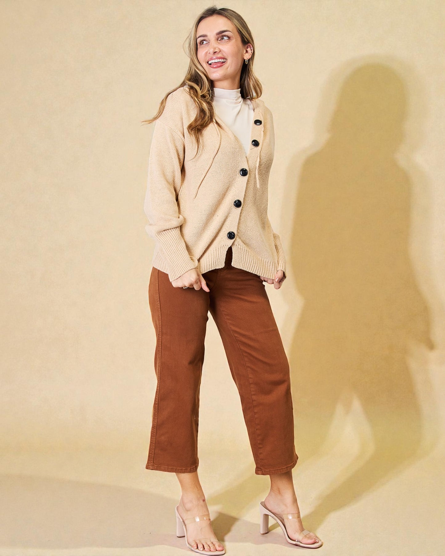 Woman wearing a beige blazer with black buttons and brown pants against a beige background