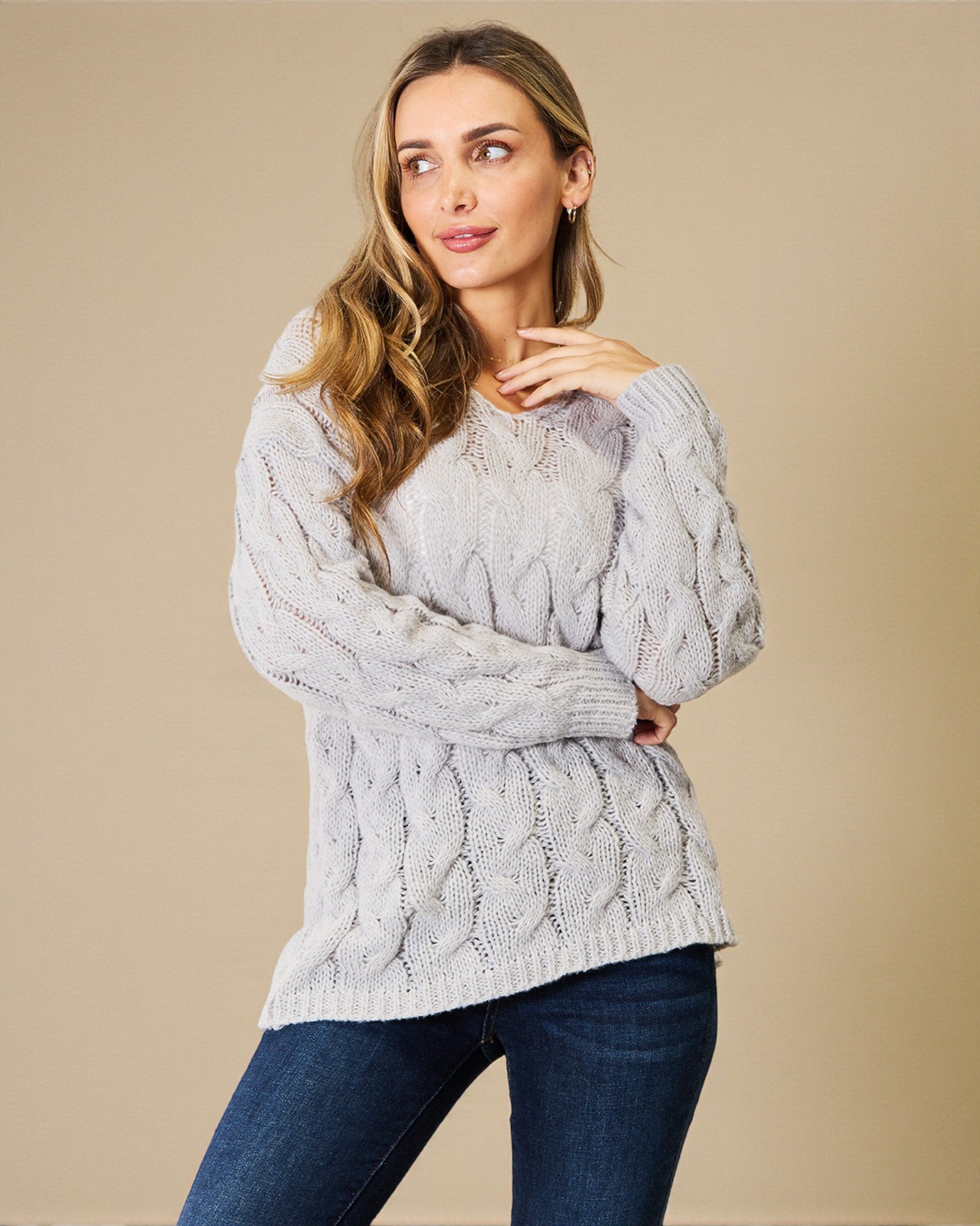 Woman wearing a gray cable knit sweater against a beige background