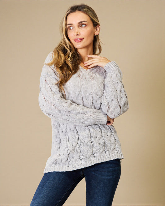 Woman wearing a gray cable knit sweater against a beige background