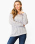 A woman wearing a light gray cable-knit sweater and dark blue jeans, posing against a plain white studio background.