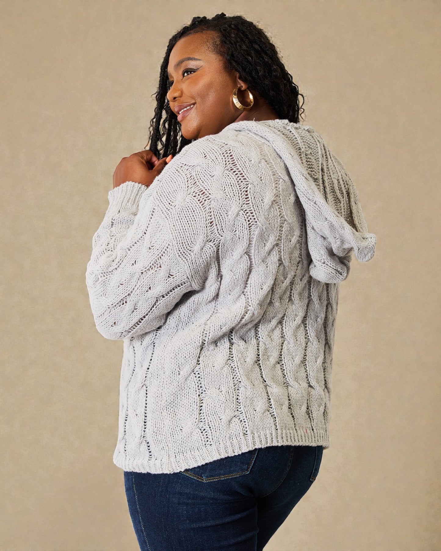 Woman wearing a cable knit sweater against a beige background