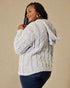 Woman wearing a cable knit sweater against a beige background