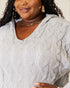 Woman wearing a gray cable knit sweater with a neutral background