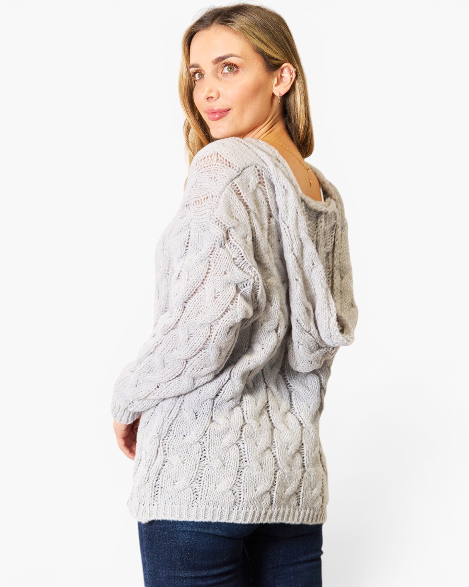 A woman wearing a light gray cable-knit hooded sweater, shown from a three-quarter back view against a plain white studio background.