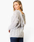 A woman wearing a light gray cable-knit hooded sweater, shown from a three-quarter back view against a plain white studio background.