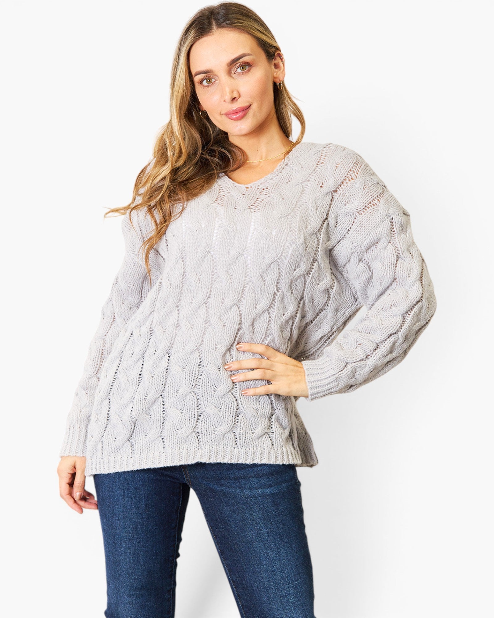 A woman modeling a light gray cable-knit sweater with balloon sleeves, paired with dark blue jeans, against a plain white studio background.