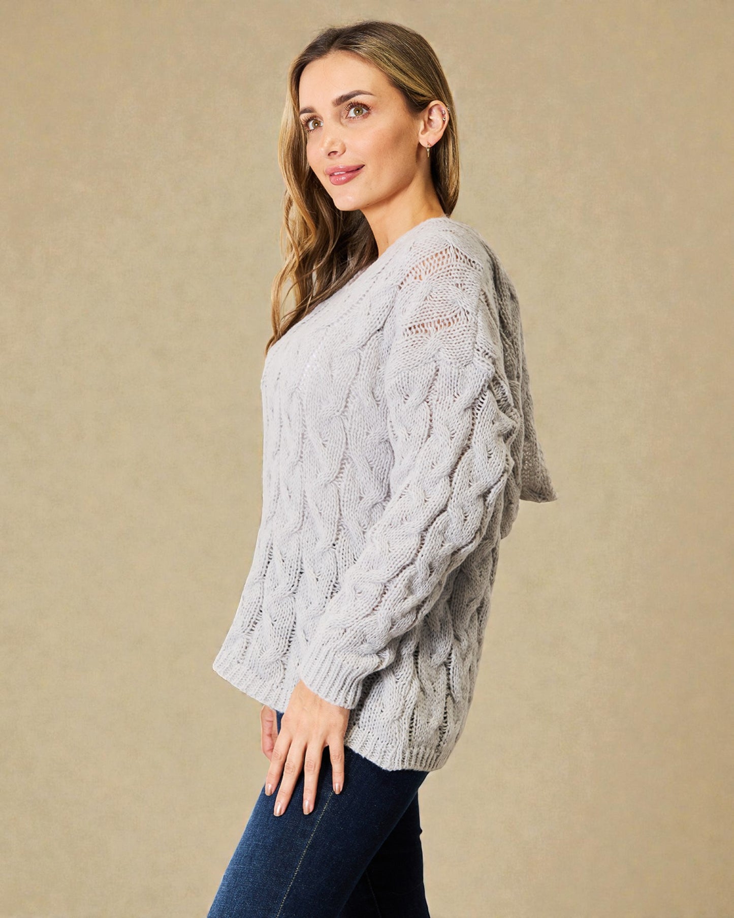 Woman wearing a gray cable knit sweater against a beige background