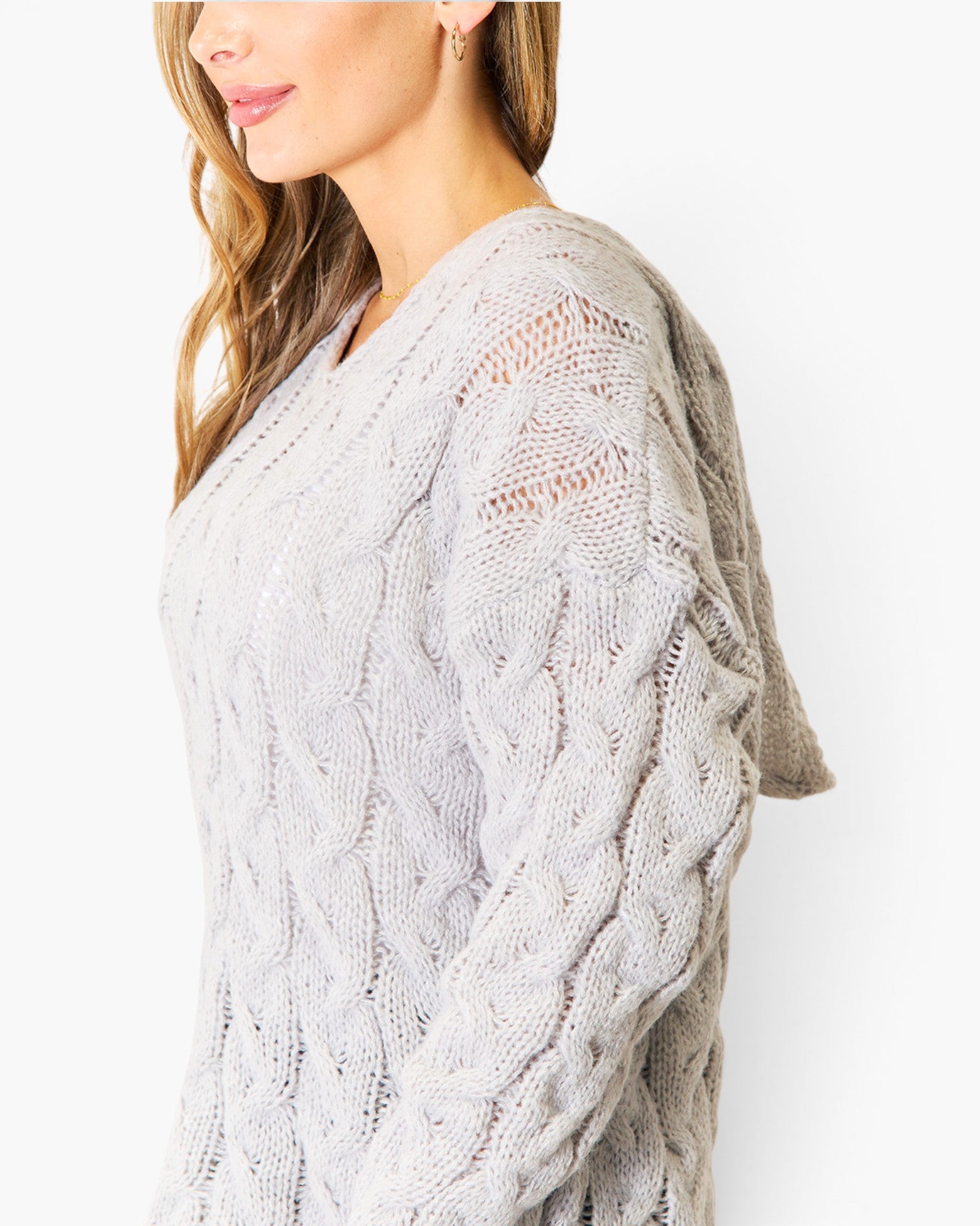 A woman wearing a light gray cable-knit sweater, shown from a side profile against a plain white background.