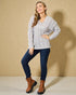 Woman wearing a gray cable knit sweater, blue jeans, and brown boots against a beige background