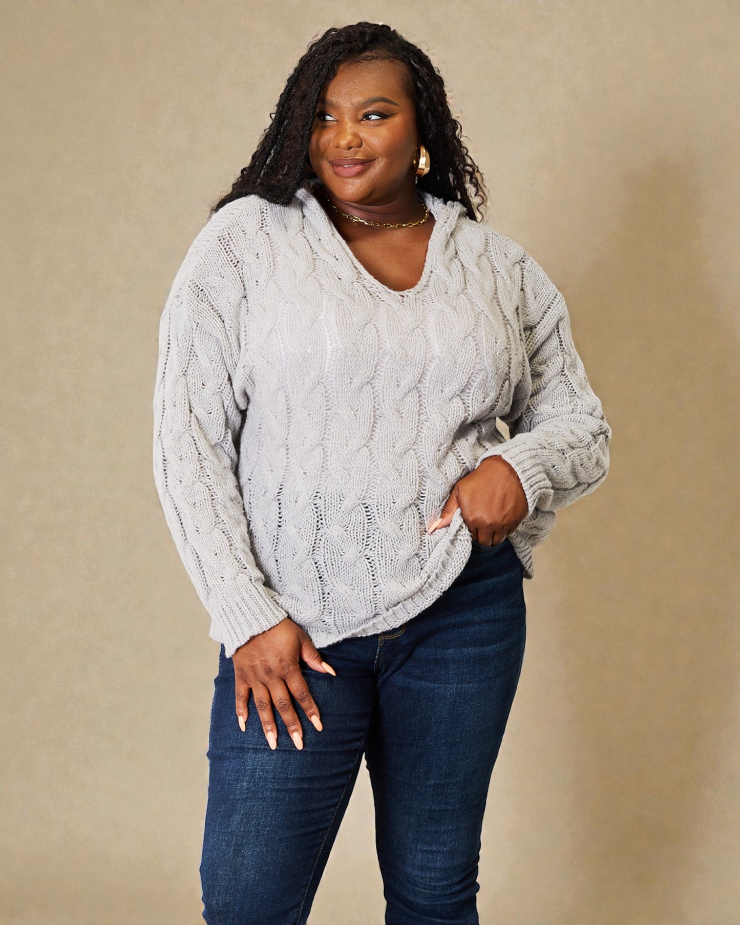 Woman wearing a cable knit sweater and jeans against a beige background