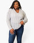 A woman modeling a light gray cable-knit sweater with a V-neck and long sleeves, paired with dark blue jeans, against a plain white background.