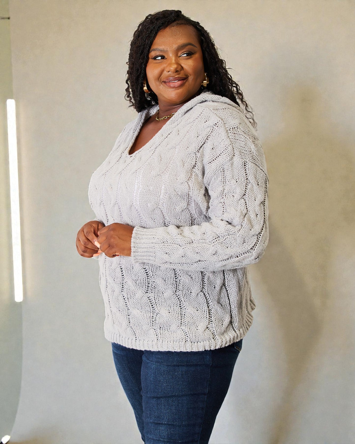 Woman wearing a white cable knit sweater and dark jeans against a plain background