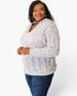 A woman modeling a light gray cable-knit hooded sweater with blue jeans, photographed against a clean white studio background.