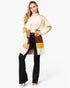 A woman modeling a long, open-front color-block cardigan with cream, mustard yellow, tan, and brown panels, worn over a white mock-neck top and black flared pants, against a plain white studio background.