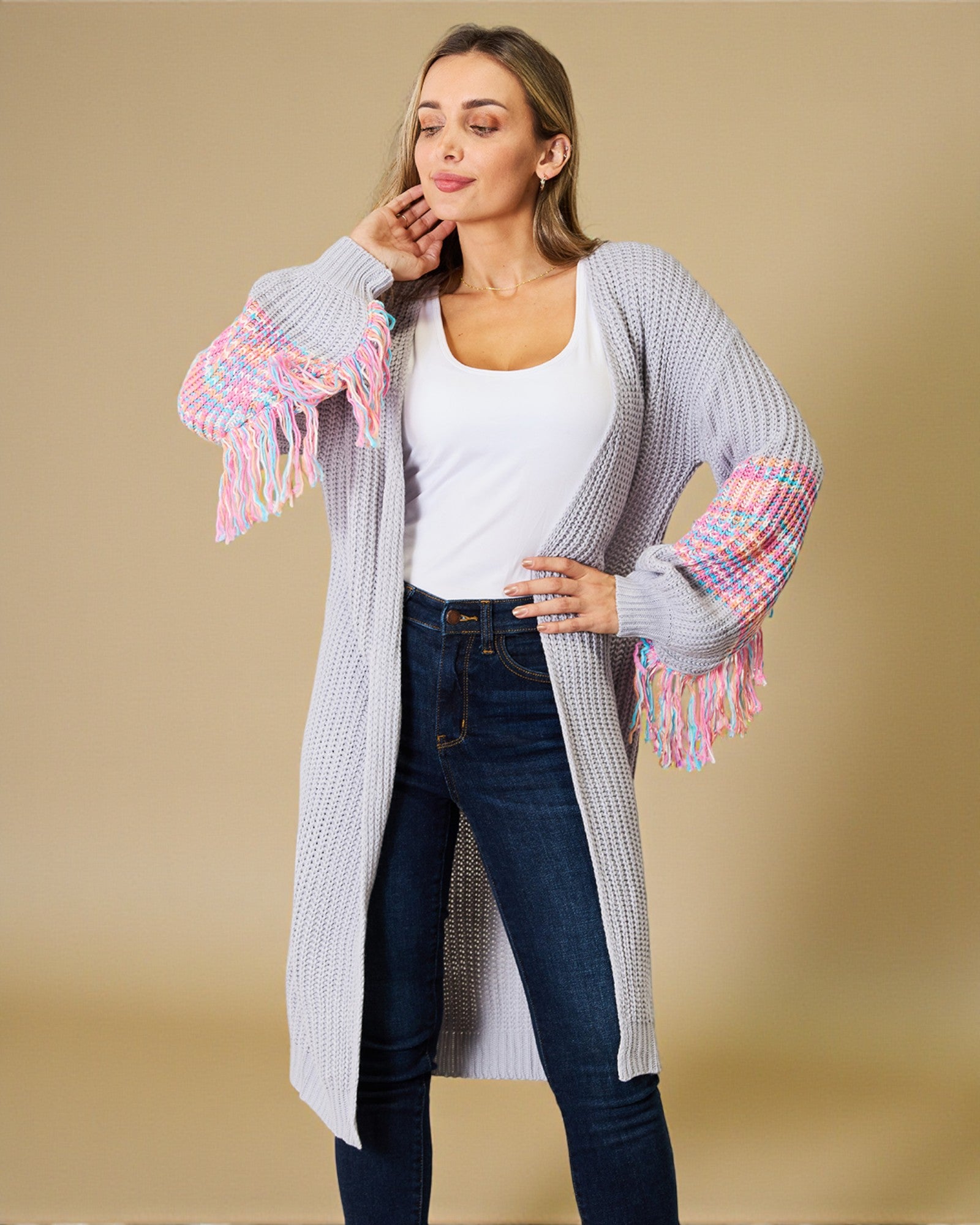 Woman wearing a long, light gray cardigan with colorful fringe sleeves on a beige background