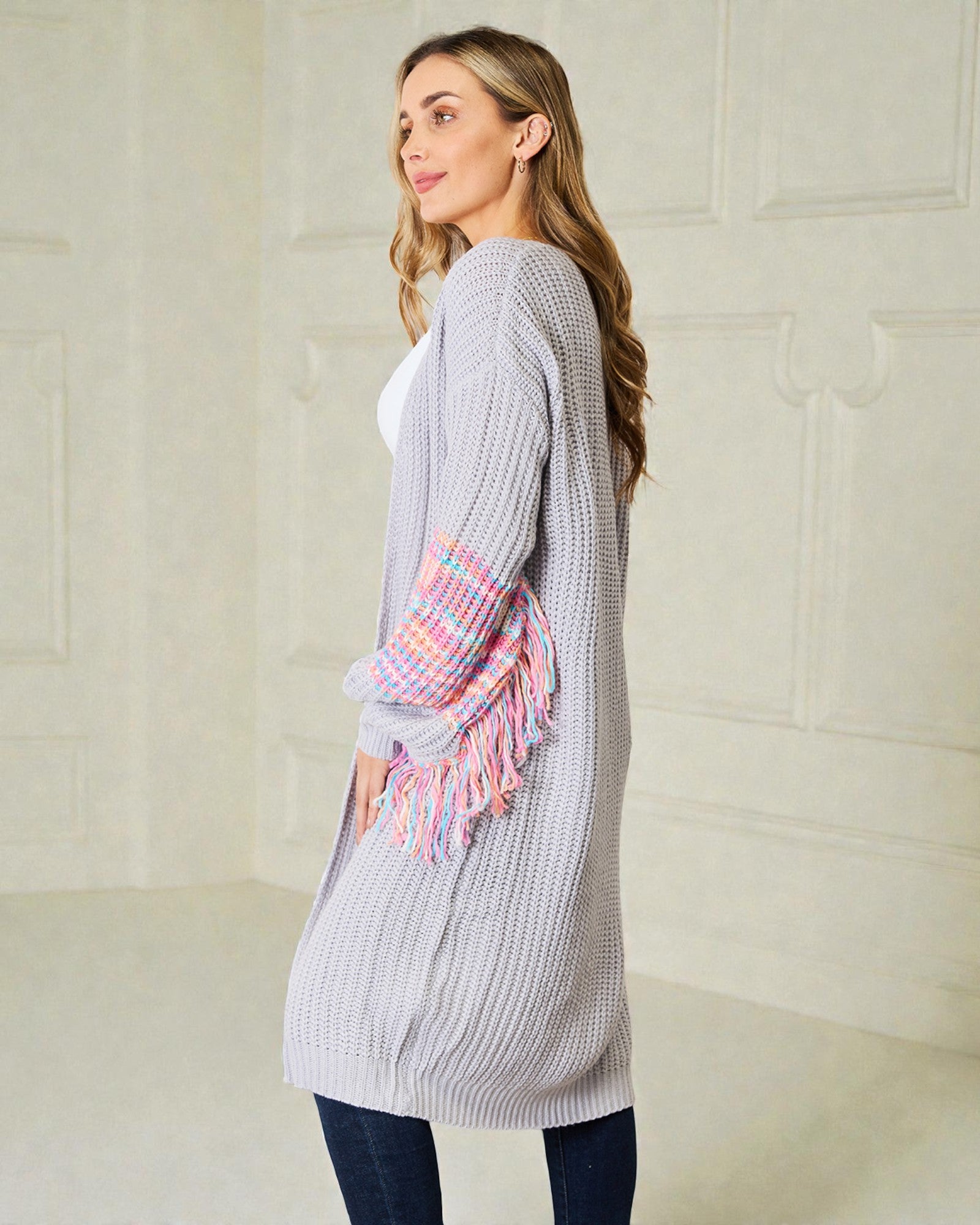 Woman wearing a long gray cardigan with a colorful scarf over her shoulder against a light background