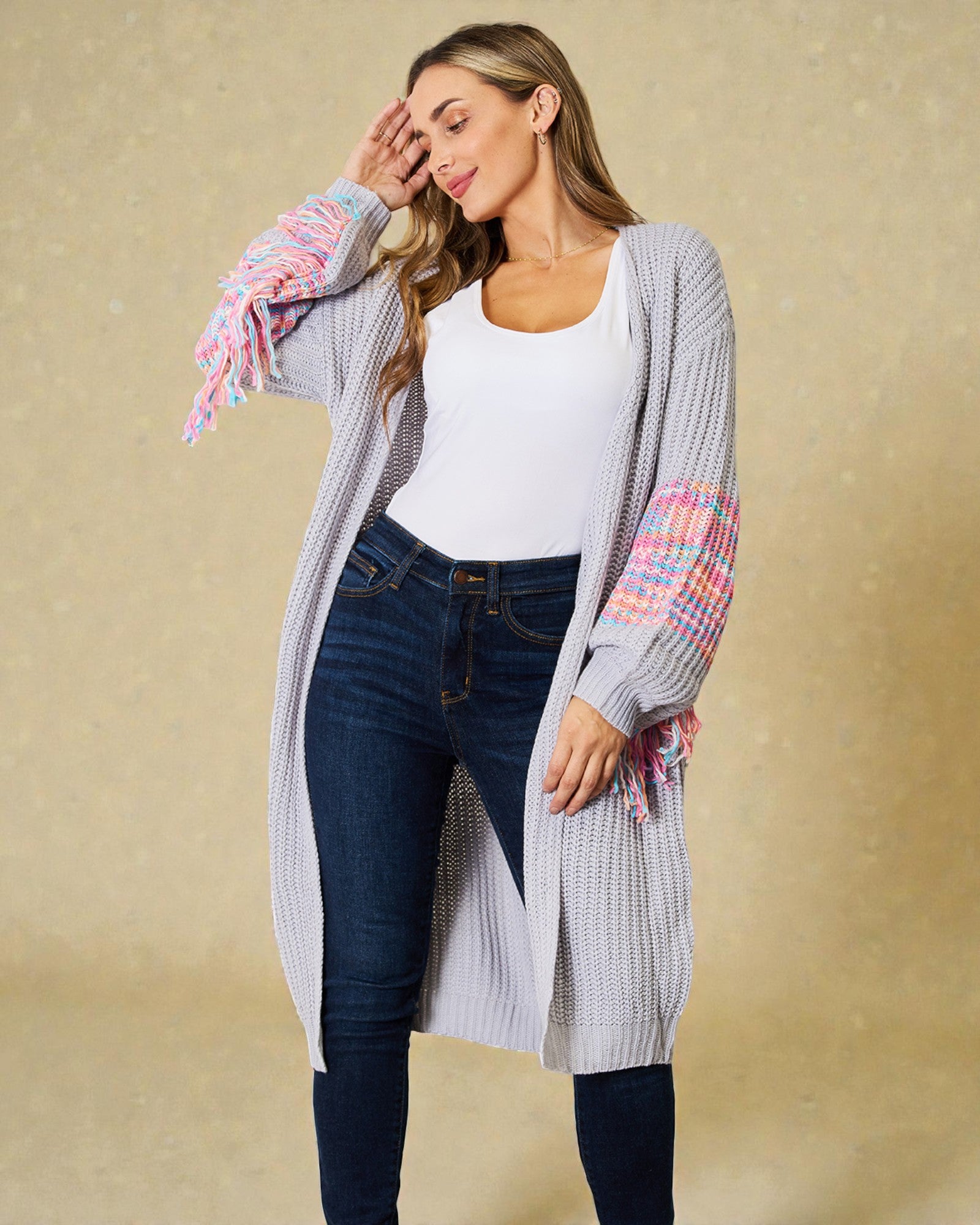 Woman wearing a long, light gray cardigan with colorful sleeves against a beige background