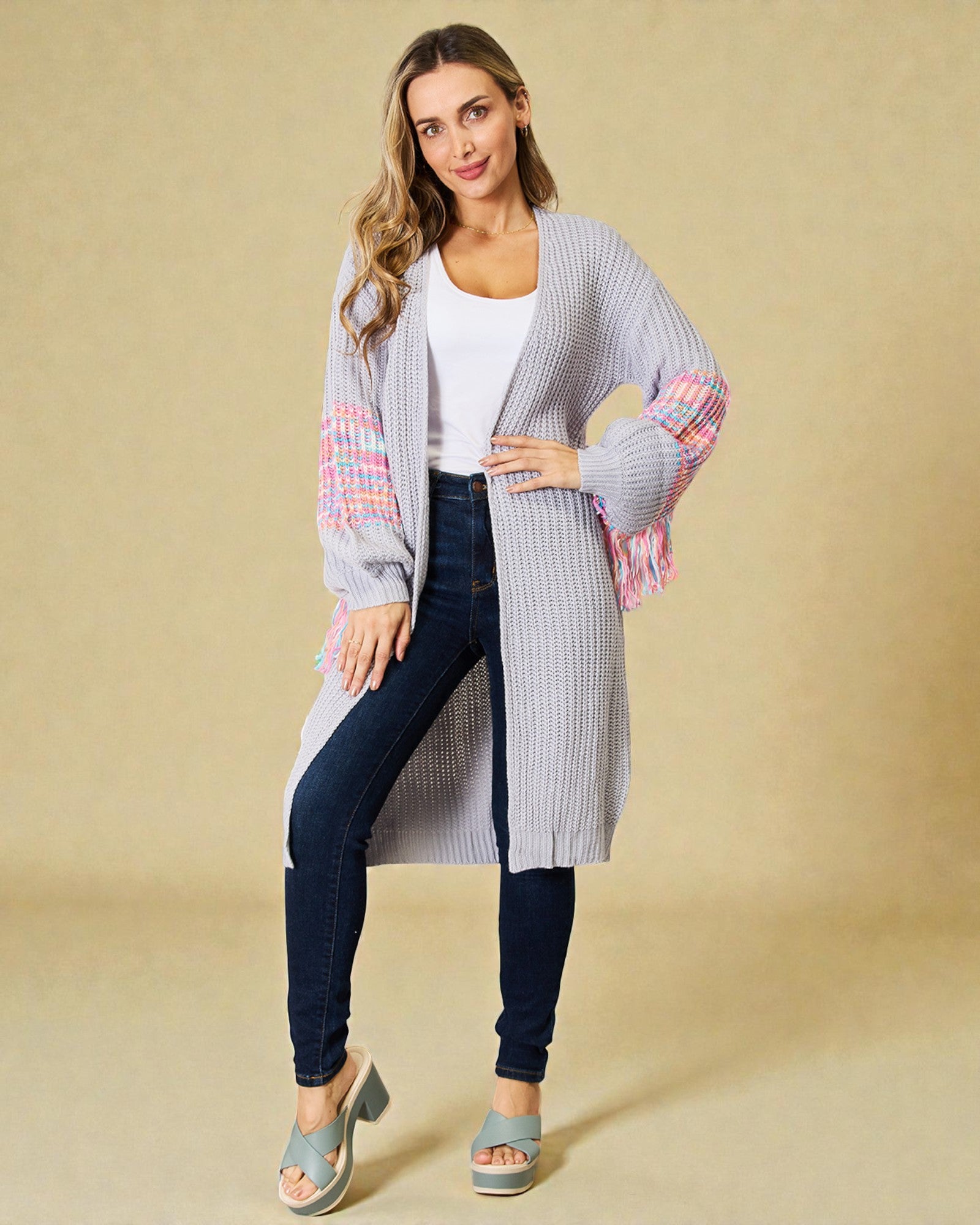Woman wearing a long, light gray cardigan with colorful sleeves on a beige background