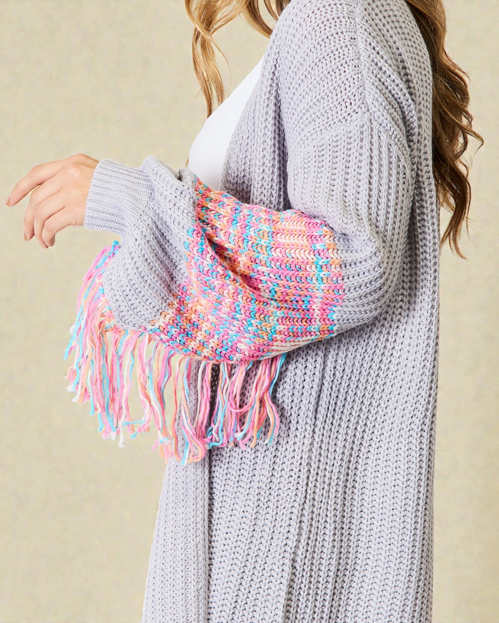 Person wearing a gray knit cardigan with a colorful scarf draped over the shoulder against a beige background