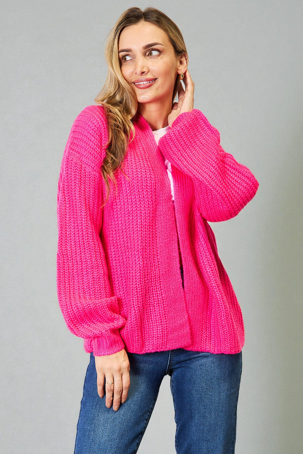 Woman wearing a bright pink knitted cardigan against a gray background