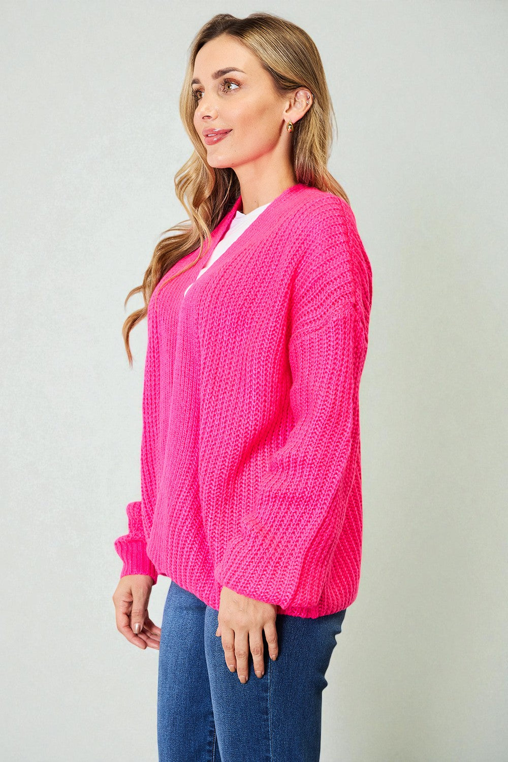 Woman wearing a bright pink cardigan over a white shirt on a plain background