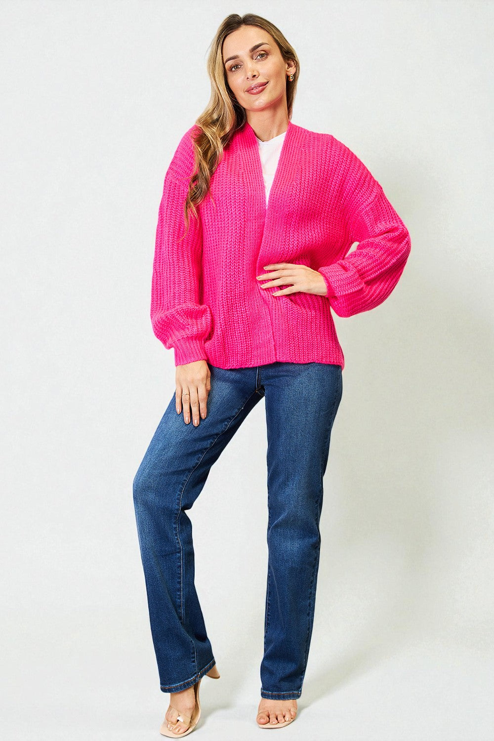 Woman wearing a bright pink cardigan and blue jeans on a white background