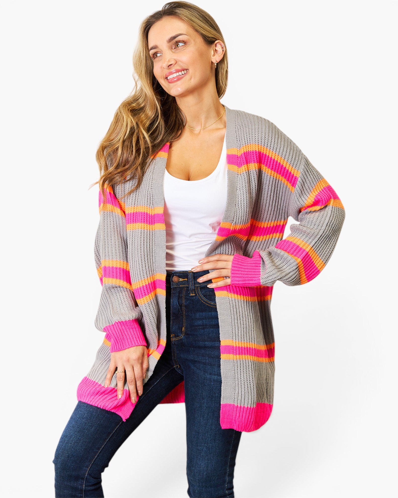 A woman modeling a gray open-front cardigan with bright pink and orange horizontal stripes, worn over a white tank top and blue jeans against a light gray studio background.